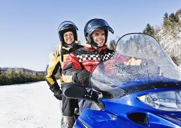 Pareja sonriendo mientras conducen una moto de nieve en Levi, Laponia, listos para un safari ártico.