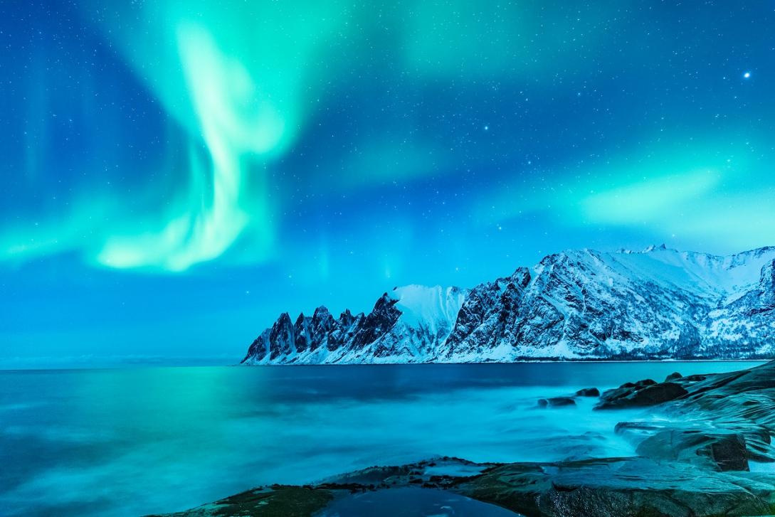 Impresionantes auroras boreales verdes sobre las montañas y el mar en un viaje por el Ártico Global.